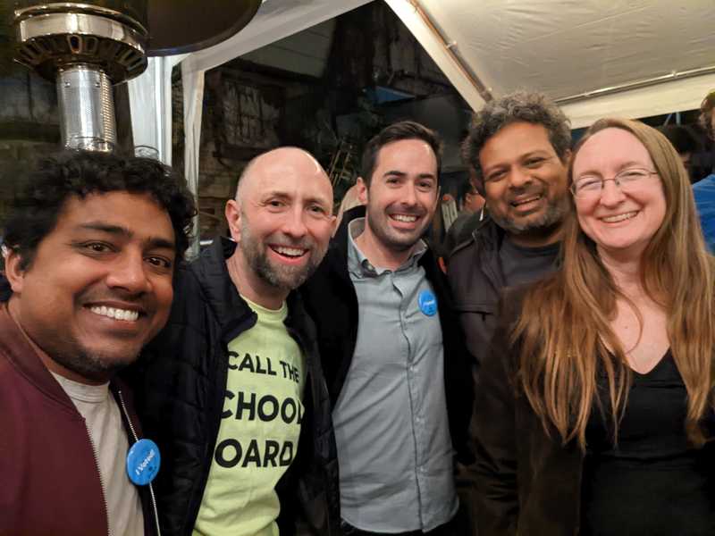 five people standing in a row, smiling, at an election night victory party